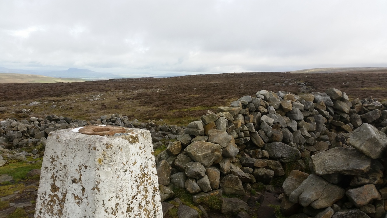 "Standing next to a survey marker, the view over moorland with hills in the distance"
